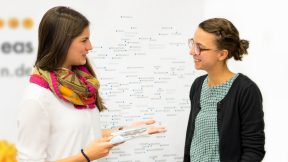 Two students talking in front of a world map hanging on the wall